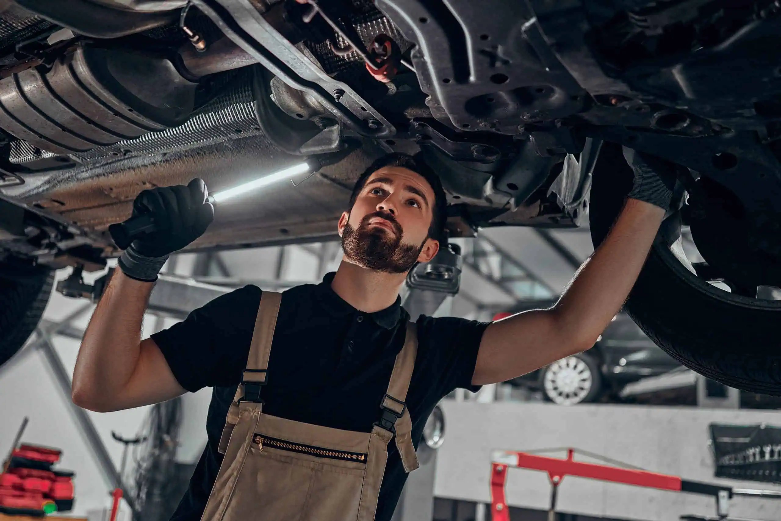 Mechanic working on car underside with flash light